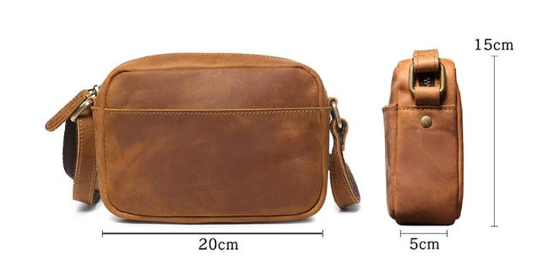 Puede incluir: Bolso bandolera de cuero marr&oacute;n, de forma rectangular, con un bolsillo frontal. El bolso mide 20 cm de largo, 15 cm de alto y 5 cm de ancho. Tiene una correa para el hombro y herrajes met&aacute;licos.