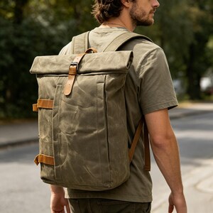 Puede incluir: Mochila de lona verde oliva con correas y hebilla de cuero marrón. El diseño enrollable tiene una solapa frontal y correas ajustables. Una bolsa duradera y elegante para el uso diario.