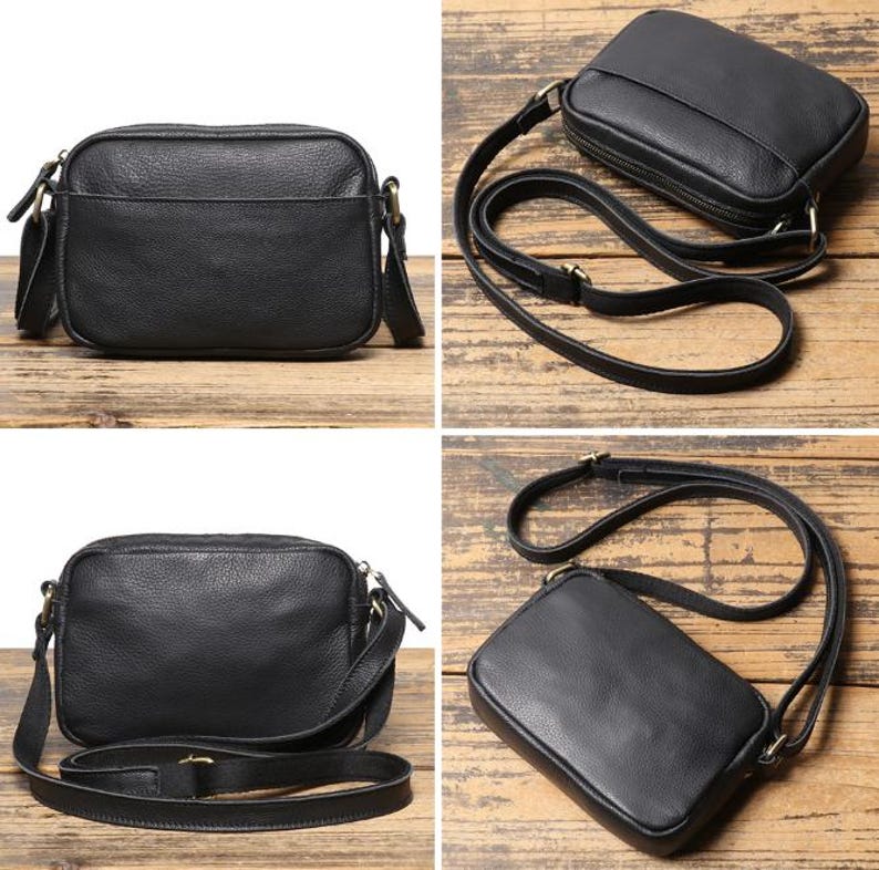 Puede incluir: Bolso bandolera de cuero negro con forma rectangular y correa larga ajustable. El bolso cuenta con un compartimento principal con cremallera y un peque&ntilde;o bolsillo exterior. Los herrajes son dorados y el bolso se muestra sobre una superficie de madera.