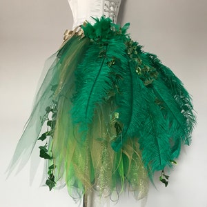 May include: A green tulle skirt with gold glitter and green feathers. The skirt is decorated with green ivy and has a white corset top.