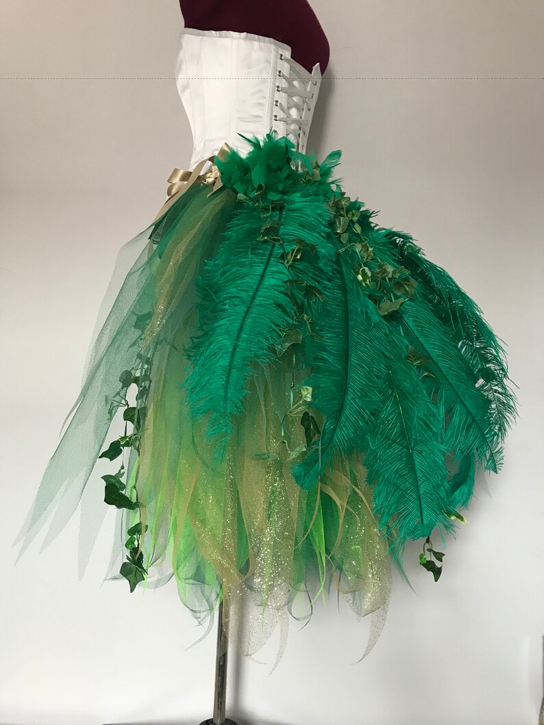 May include: A green tulle skirt with gold glitter and green feathers. The skirt is decorated with green ivy and has a white corset top.