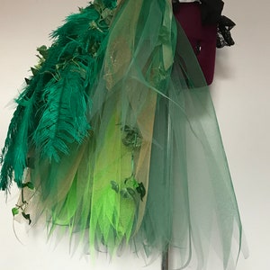 May include: A green, gold, and lime green tulle skirt with green feathers and ivy accents. The skirt is layered and has a flowing, whimsical design.