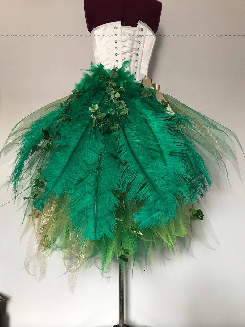 May include: A green tulle skirt with green feathers and green leaves. The skirt is on a white dress form.