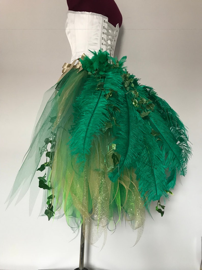 May include: A green tulle skirt with gold glitter and green feathers. The skirt is decorated with green ivy and has a white corset top.