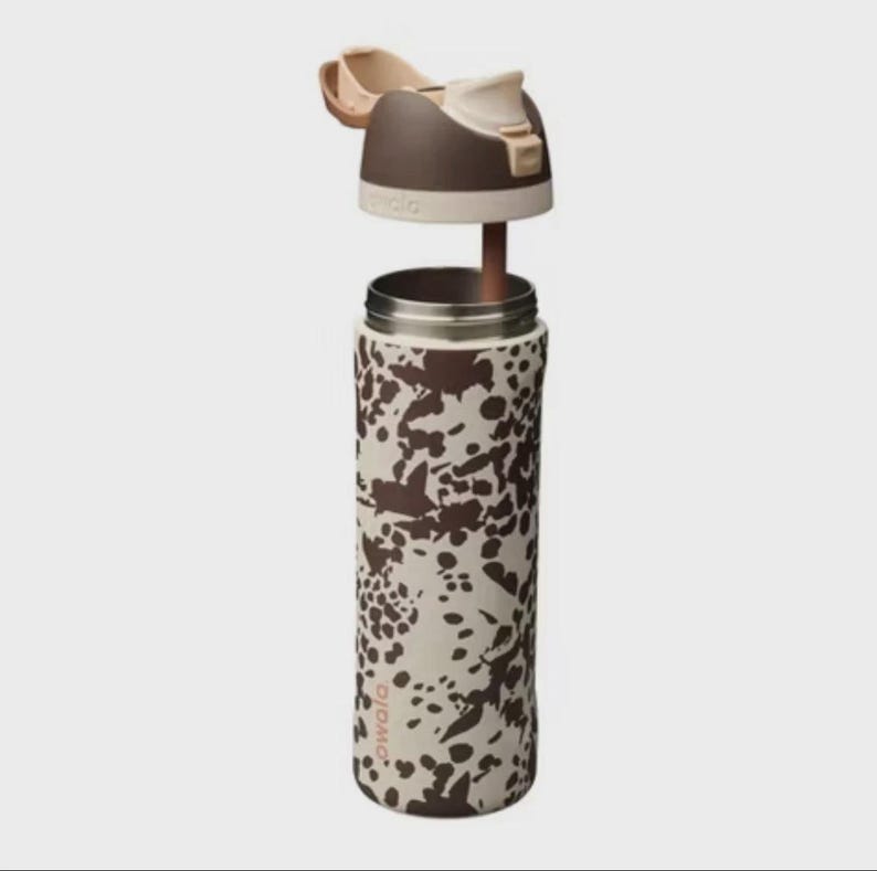 May include: A stainless steel water bottle with a brown and cream cow print design. The lid is open, revealing the interior. The lid is brown and cream with a flip-top opening. The bottle is cylindrical and has a silver rim.