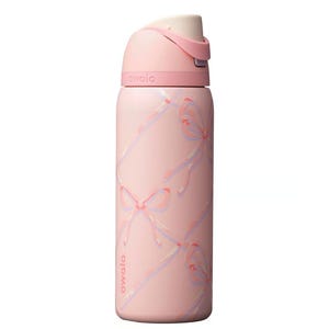 Op de afbeelding: Een roze Owala waterfles met een strikpatroon. De fles heeft een klapdeksel en een handvat. De body van de fles is lichtroze met een herhalend patroon van roze en paarse strikken. Het woord "owala" staat op de fles.