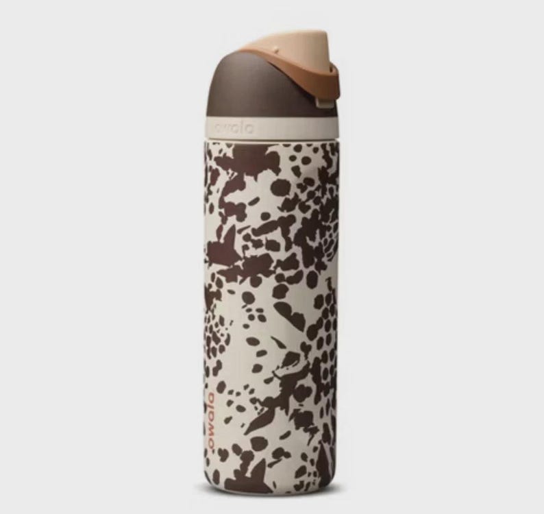 May include: A tall, insulated Owala water bottle with a brown and cream spotted pattern. The bottle has a dark brown lid and a tan carrying handle. The Owala logo is printed on the side of the bottle.