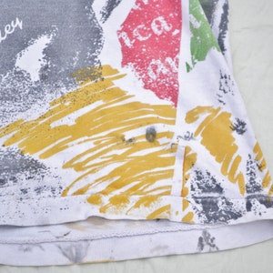 May include: A white t-shirt with a colorful abstract print featuring yellow, red, green, and gray paint splatters. The text "Bob Marley" is printed in black on the shirt.