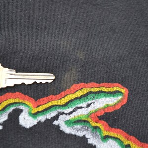 K&ouml;nnte beinhalten: Schwarzes T-Shirt mit einem bunten Grafikdruck eines Gebirges. Die Grafik ist in Rot-, Gelb-, Gr&uuml;n- und Wei&szlig;t&ouml;nen gehalten.