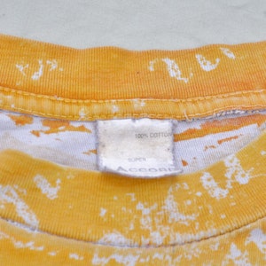 May include: A yellow and white tie-dye t-shirt with a white tag that reads "100% cotton, Super, Accord".