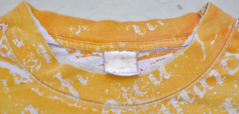 May include: A yellow and white tie-dye t-shirt with a white tag that reads "100% cotton, Super, Accord".