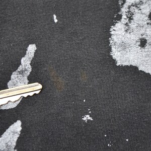 K&ouml;nnte beinhalten: Nahaufnahme eines schwarzen T-Shirts mit einem verblassten wei&szlig;en Druck. Das Shirt hat einen kleinen braunen Fleck.