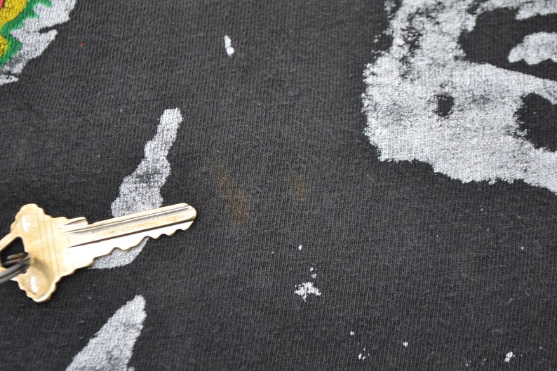 K&ouml;nnte beinhalten: Nahaufnahme eines schwarzen T-Shirts mit einem verblassten wei&szlig;en Druck. Das Shirt hat einen kleinen braunen Fleck.