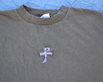 May include: A dark gray t-shirt with a blue and yellow embroidered cross on the front.
