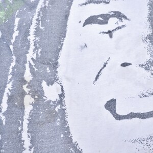May include: Close-up of a white t-shirt with a black and white graphic print of a person's face. The print is faded and distressed, giving it a vintage look.