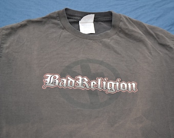 May include: A dark gray t-shirt with a graphic of a circle with a cross inside and the text "Bad Religion" in a stylized font.