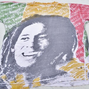 May include: A white t-shirt with a colorful print of Bob Marley's face. The print features the colors red, yellow, and green, and the text "Bob Marley" is printed below the face.