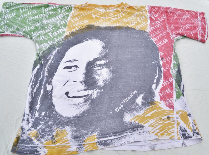 May include: A white t-shirt with a colorful print of Bob Marley's face. The print features the colors red, yellow, and green, and the text "Bob Marley" is printed below the face.