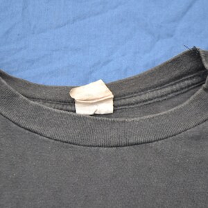 K&ouml;nnte beinhalten: Nahaufnahme des Ausschnitts eines schwarzen T-Shirts mit einem wei&szlig;en Etikett.