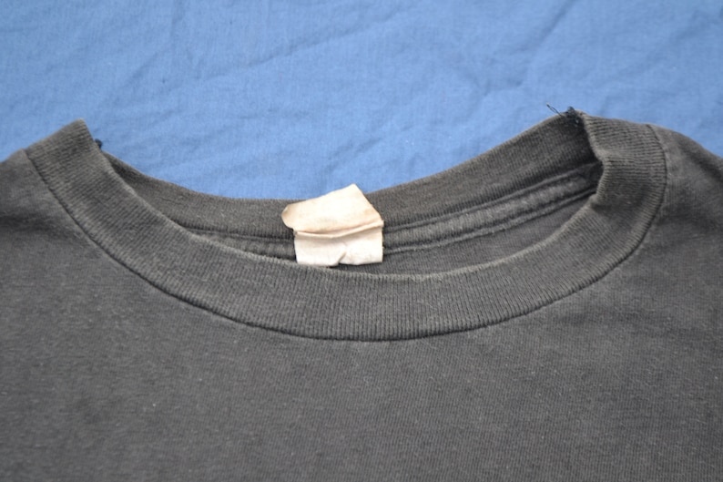 K&ouml;nnte beinhalten: Nahaufnahme des Ausschnitts eines schwarzen T-Shirts mit einem wei&szlig;en Etikett.
