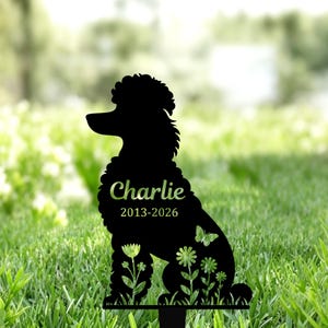 Könnte beinhalten: Schwarzer Metall-Gartenstecker mit einer Silhouette eines Pudels. Der Name "Charlie" und die Daten "2013-2026" sind abgebildet. Das Design umfasst Blumen- und Schmetterlingsakzente, geeignet für eine Haustier-Gedenkstätte.