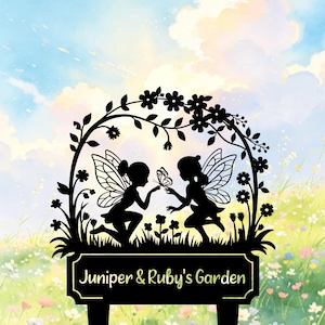 May include: Black metal garden stake with two fairy silhouettes, butterfly wings, and a butterfly. The design includes floral accents and the text "Juniper & Ruby's Garden" on a rectangular plaque. The background shows a sky and a flower garden.