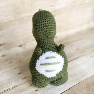 May include: Green crocheted dinosaur toy with a white crocheted patch on its back.
