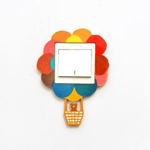 May include: A white light switch cover plate featuring a painted hot air balloon design. The balloon is composed of colorful circular shapes in red, orange, yellow, blue, and brown, with a small brown bear figure inside the orange basket.