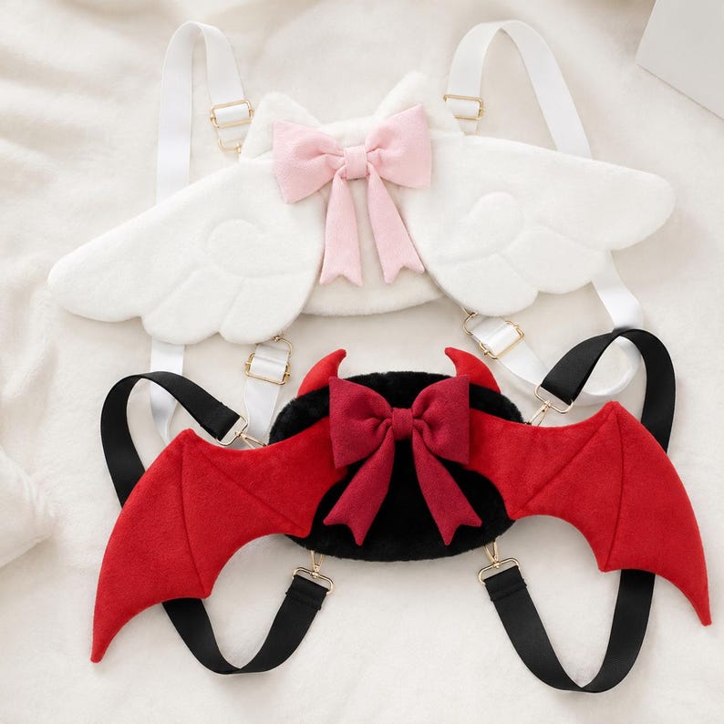 May include: Two novelty backpacks, one white with angel wings and a pink bow, the other black with red devil wings and a red bow. Both have adjustable straps and gold-colored hardware.