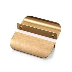 Può includere: Due maniglie per mobili color oro con un design curvo. Le maniglie hanno una finitura spazzolata e sono mostrate su uno sfondo bianco. Ogni maniglia ha due fori preforati per il montaggio.