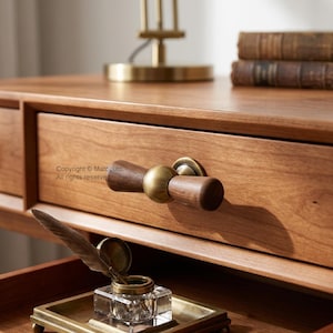 May include: A wooden drawer front featuring a horizontal handle made of two dark wood cylindrical pieces connected by a central brass sphere. Below, a glass inkwell with a feather quill sits on a brass tray. Text reads Copyright MatoLulu.
