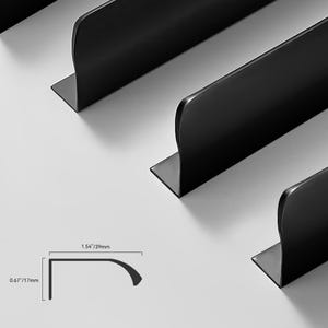 Puede incluir: Tres perfiles de borde de metal negro mate en forma de L con un borde superior curvo. Un diagrama técnico muestra las dimensiones del perfil como 39 mm de ancho y 17 mm de alto, ilustrando la sección transversal específica del borde metálico.