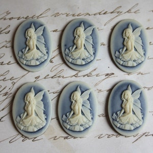 May include: Six oval-shaped, blue and white cameo pendants featuring a fairy design. Each pendant has a white fairy with wings and a white dress, set against a blue background.