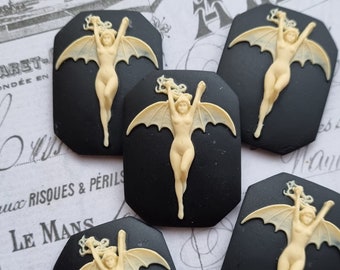 May include: Five black and white cameo-style buttons with a raised image of a woman with wings. The woman is in a flying pose with her arms outstretched. The buttons are approximately 1 inch in diameter.