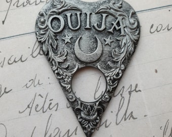 May include: A silver-colored metal Ouija board pendant in the shape of a heart with a crescent moon and two stars. The word "OUIJA" is embossed on the pendant.