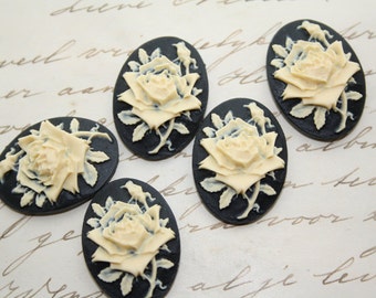 May include: Five black cameo-style oval-shaped buttons with a raised white design of a rose. The roses are detailed with leaves and stems.