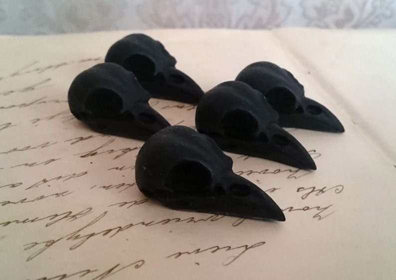 May include: Five small black bird skulls, made of resin, are arranged on a piece of paper with handwritten text.