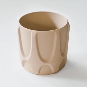 May include: A beige cylindrical planter with a textured, geometric design. The planter has a wide opening and a series of vertical, curved indentations around its exterior. The neutral color and modern design make it suitable for various plants.