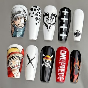 May include: A set of ten long, coffin-shaped false nails. The nails feature various designs, including anime characters, a skull and crossbones, flames, and the text "ONE PIECE". Colors include white, black, red, yellow, and orange.