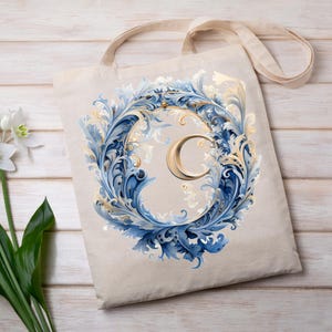 Puede incluir: Bolso tote beige con un dise&ntilde;o decorativo. El dise&ntilde;o presenta la letra "C" dorada rodeada por una corona de elementos florales azules y dorados. El bolso tiene un asa simple y est&aacute; hecho de una tela de color natural.
