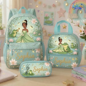 May include: A light blue backpack, lunch bag, and pencil case set featuring a princess in a green gown, a green alligator, and a small insect. Each item is decorated with water lilies and the name Sophia in gold script lettering.