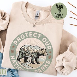 Sand colored sweatshirt with "Protect Our National Parks" circular graphic.