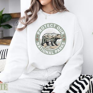 White sweatshirt with "Protect Our National Parks" circular graphic featuring a bear.