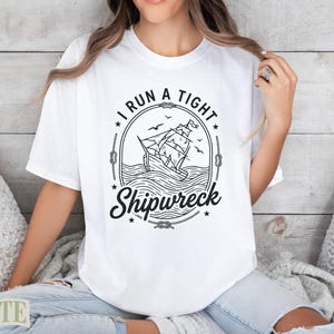 White t-shirt with a graphic featuring a sailing ship and the text "I run a tight shipwreck."