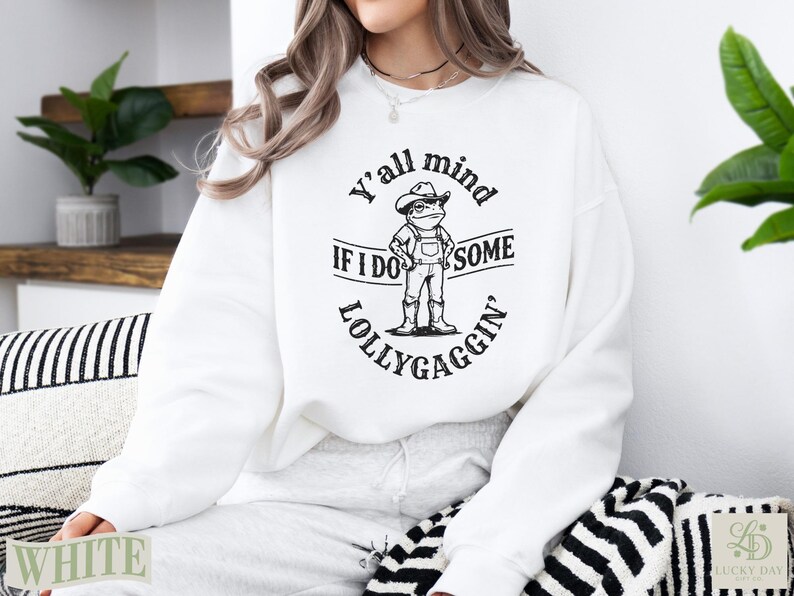 White sweatshirt with a frog wearing a cowboy hat and overalls, text reads "Y'all mind if I do some lollygaggin'".