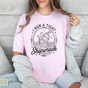 Pink t-shirt with "I RUN A TIGHT SHIPWRECK" text and a sailing ship graphic.