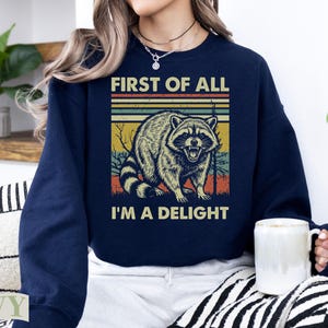 Navy sweatshirt with vintage raccoon graphic and text "FIRST OF ALL I'M A DELIGHT".