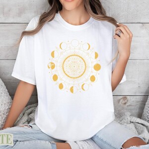 White t-shirt with yellow sun and moon phase mandala graphic.
