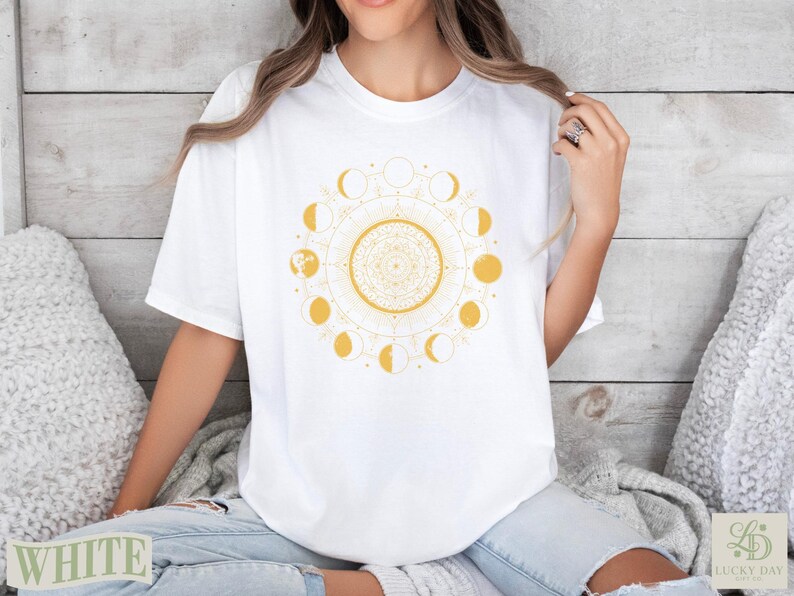 White t-shirt with yellow sun and moon phase mandala graphic.