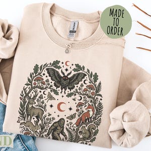 Cream sweatshirt with woodland creature and celestial art, "Made to Order" text.